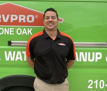 Hispanic male smiling wearing a black Servpro polo and kahki pants. Green Servpro van as a background